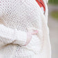 Young woman wearing a ivory chunky knit acrylic and wool sweater. This sweater has front pockets and features an open front.