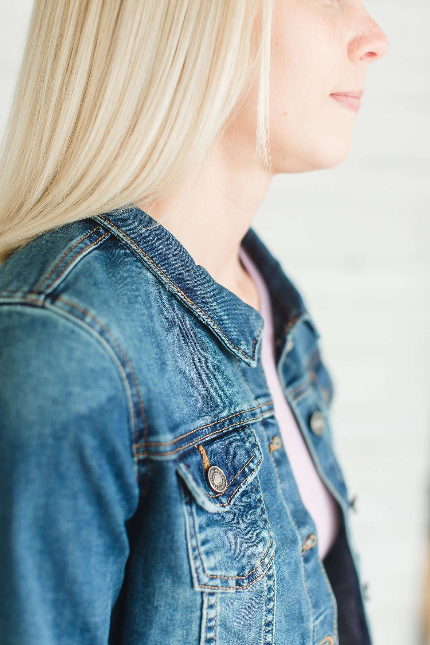 Woman wearing a long sleeve button up jean jacket with pockets and a distressed detail.