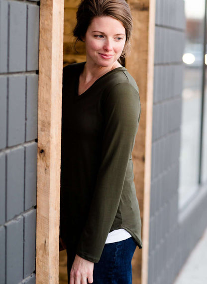 Woman wearing a long sleeve tee that is perfect for layering. It is a stretch material v-neck with a rounded hem. It comes in navy, olive, black, mustard and ivory.