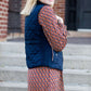 Woman wearing a cold weather, quilted puffer vest. This vest comes in mauve, black, navy and wine. It features pockets and a front zip.