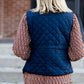 Woman wearing a cold weather, quilted puffer vest. This vest comes in mauve, black, navy and wine. It features pockets and a front zip.