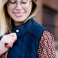 Woman wearing a cold weather, quilted puffer vest. This vest comes in mauve, black, navy and wine. It features pockets and a front zip.