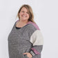 Plus size woman wearing a gray and purple hooded color block sweatshirt. It also has front pockets and banded wrist and waist.
