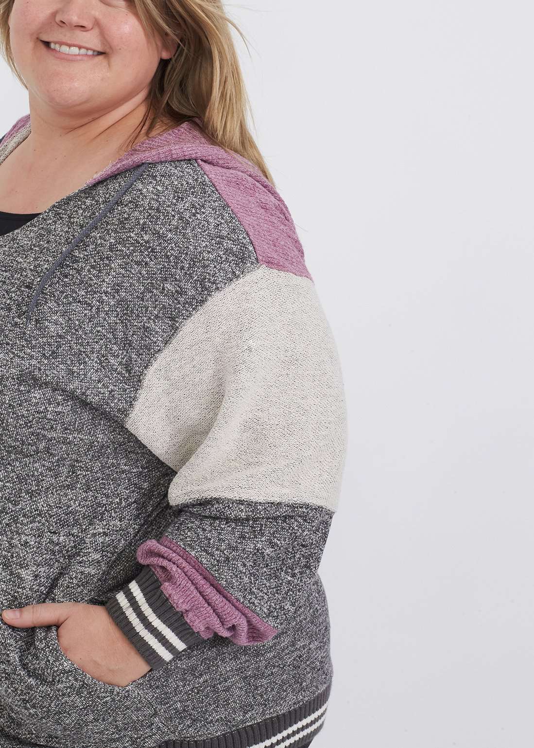 Plus size woman wearing a gray and purple hooded color block sweatshirt. It also has front pockets and banded wrist and waist.