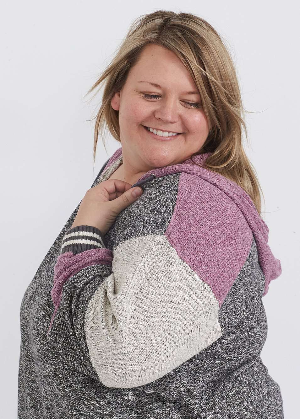 Plus size woman wearing a gray and purple hooded color block sweatshirt. It also has front pockets and banded wrist and waist.