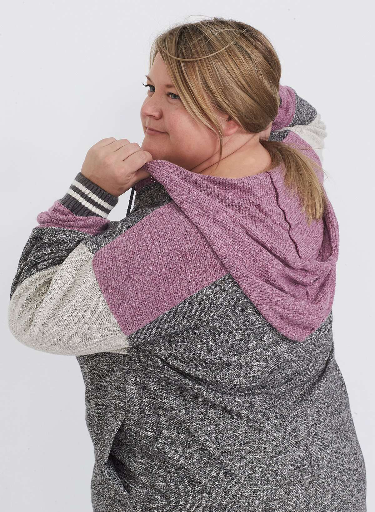 Plus size woman wearing a gray and purple hooded color block sweatshirt. It also has front pockets and banded wrist and waist.