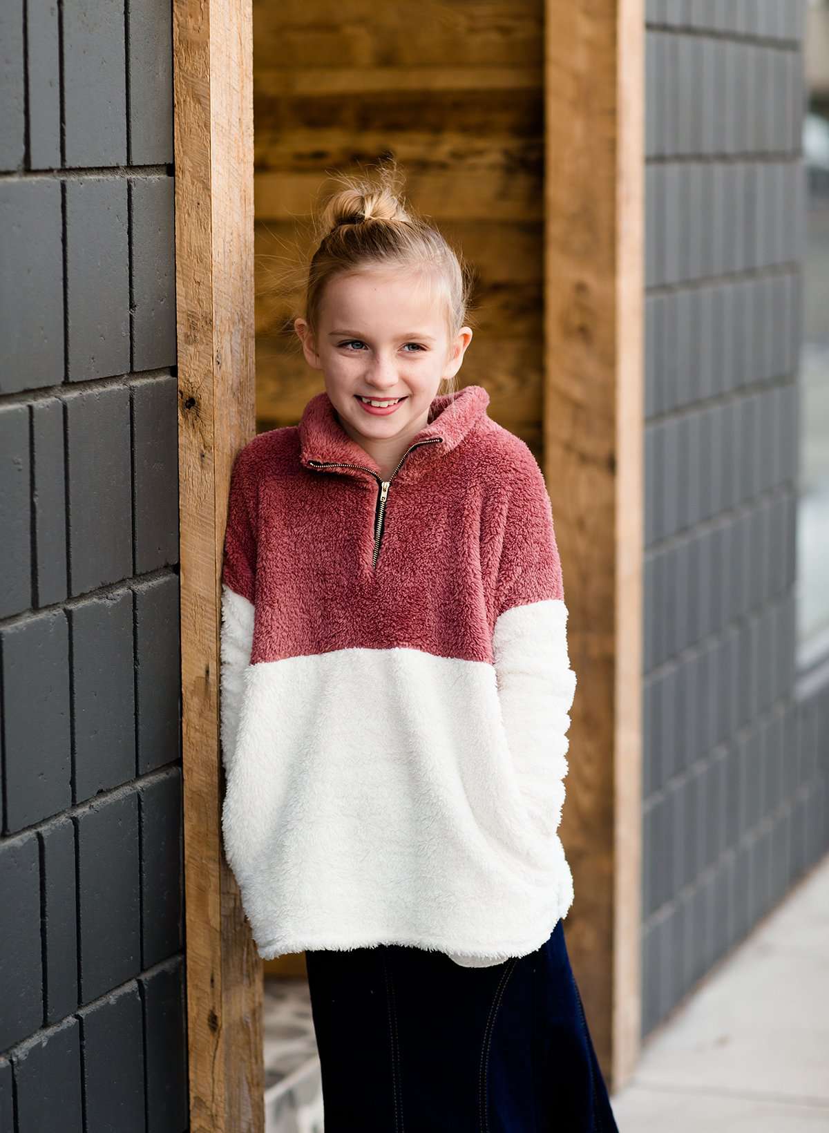 Young girl wearing a mauve and cream plush, sherpa style quarter zip sweater. This sweater has pockets and is paired with a long denim skirt. It is also a mommy and me style!