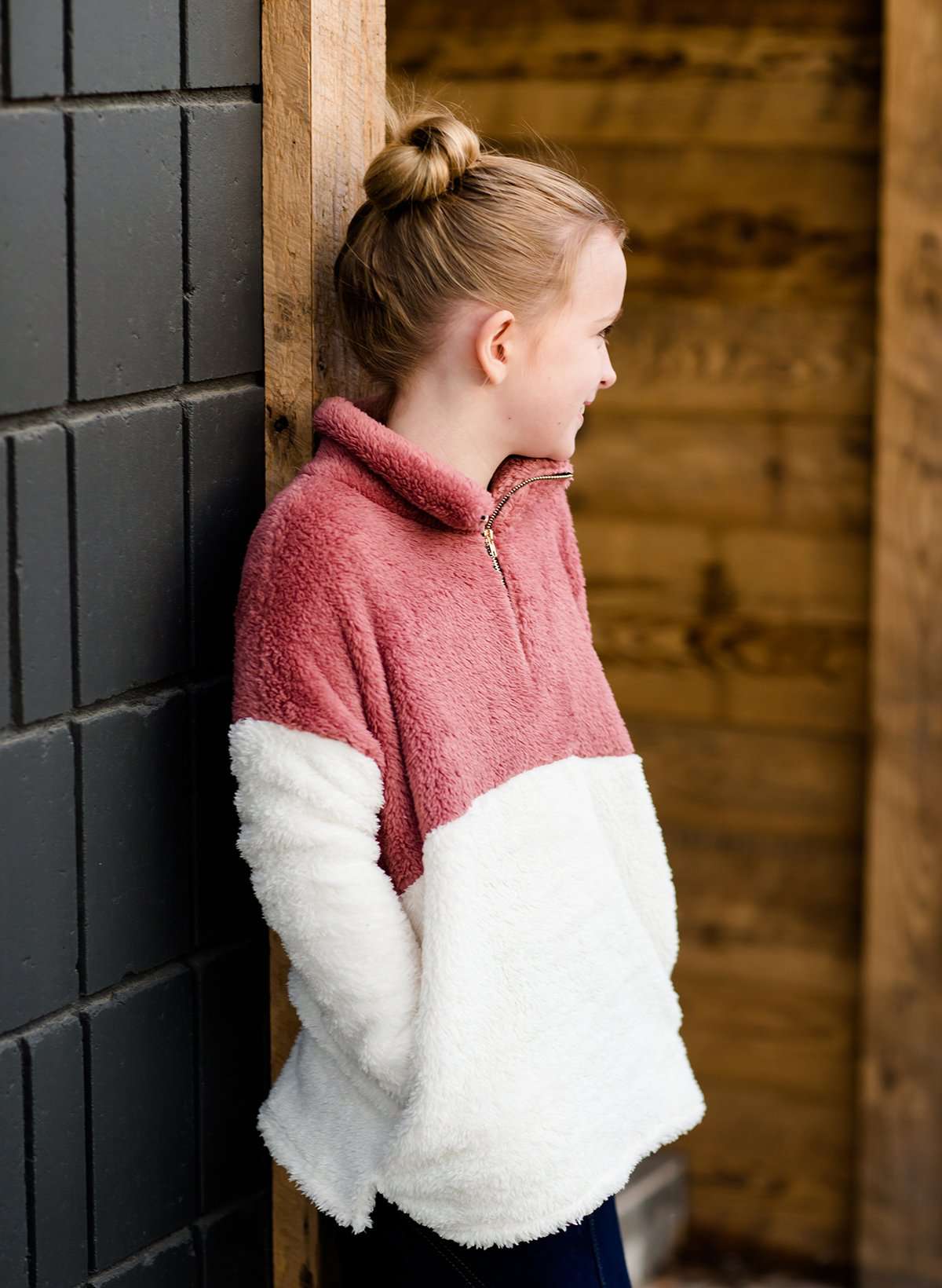 Young girl wearing a mauve and cream plush, sherpa style quarter zip sweater. This sweater has pockets and is paired with a long denim skirt. It is also a mommy and me style!