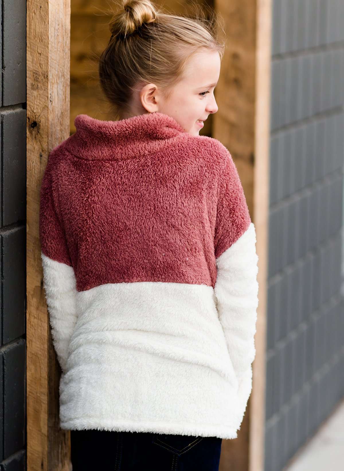 Young girl wearing a mauve and cream plush, sherpa style quarter zip sweater. This sweater has pockets and is paired with a long denim skirt. It is also a mommy and me style!