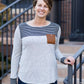 Woman wearing a gray color block stripe top with a brown, suede pocket with a button feature.