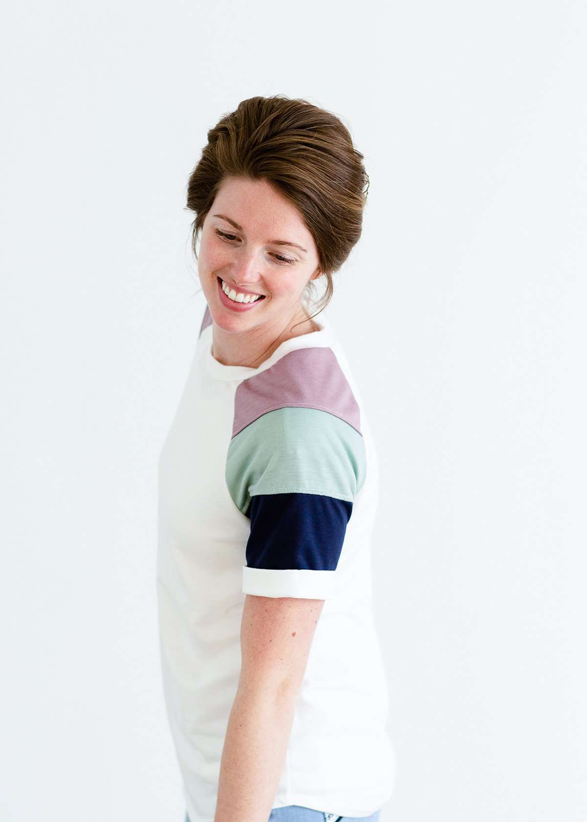 Woman wearing a modest white tee shirt with lavender, sage and navy stripes on the shoulders, tucked into a long denim modest skirt.
