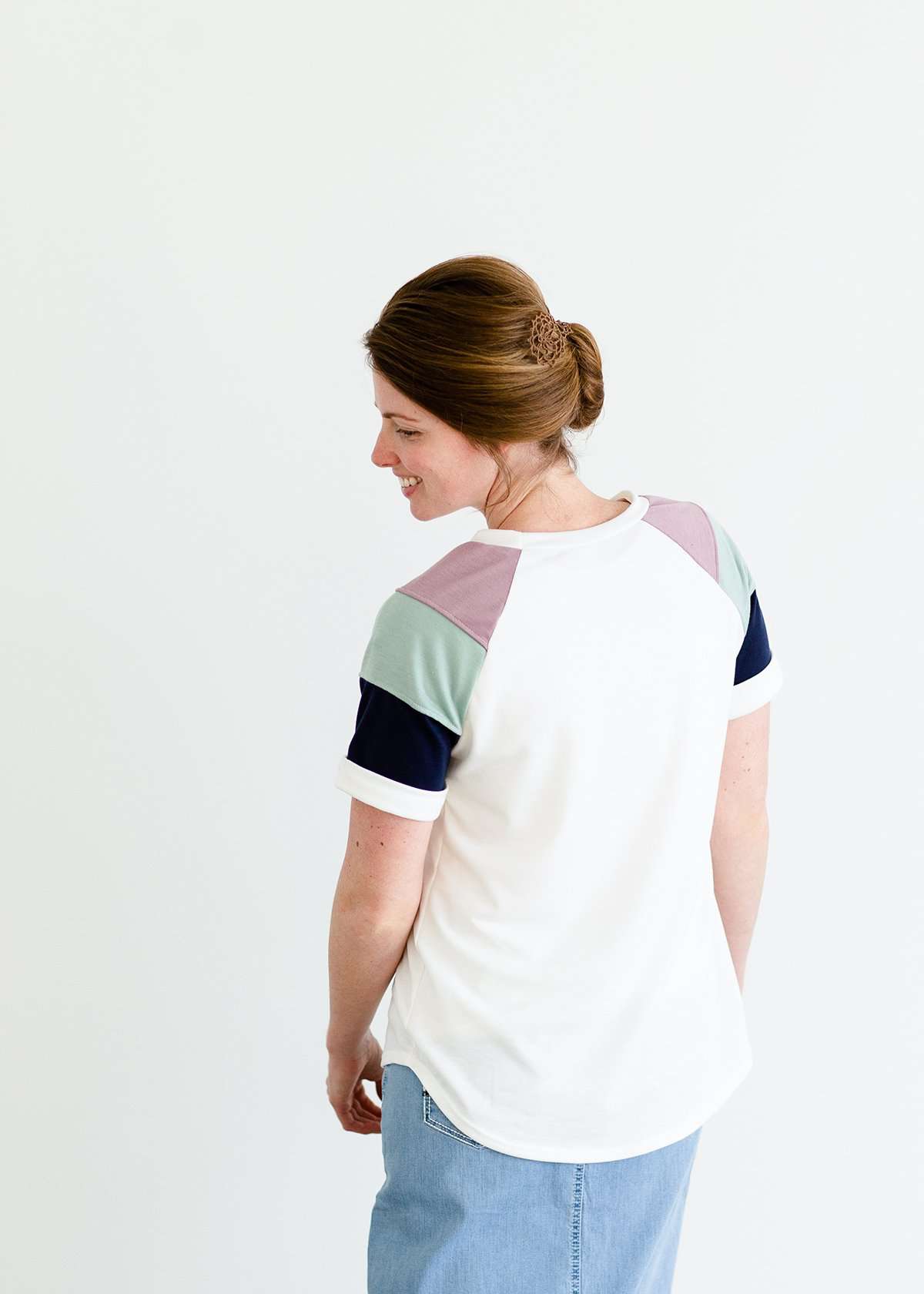 Woman wearing a modest white tee shirt with lavender, sage and navy stripes on the shoulders, tucked into a long denim modest skirt.