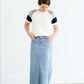 Woman wearing a modest white tee shirt with lavender, sage and navy stripes on the shoulders, tucked into a long denim modest skirt.
