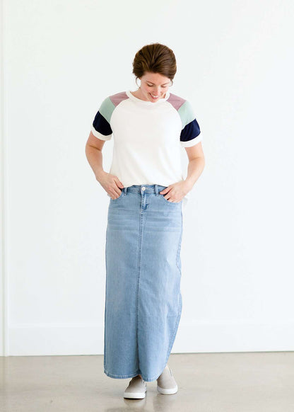 Woman wearing a modest white tee shirt with lavender, sage and navy stripes on the shoulders, tucked into a long denim modest skirt.