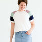 Woman wearing a modest white tee shirt with lavender, sage and navy stripes on the shoulders, tucked into a long denim modest skirt.
