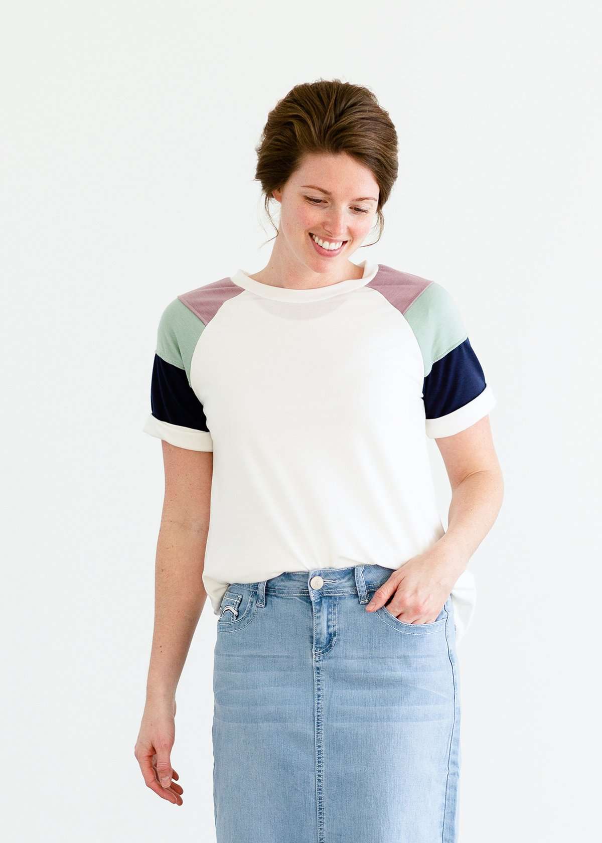 Woman wearing a modest white tee shirt with lavender, sage and navy stripes on the shoulders, tucked into a long denim modest skirt.