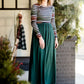 Woman wearing a striped top and solid hunter green bottom maxi dress.
