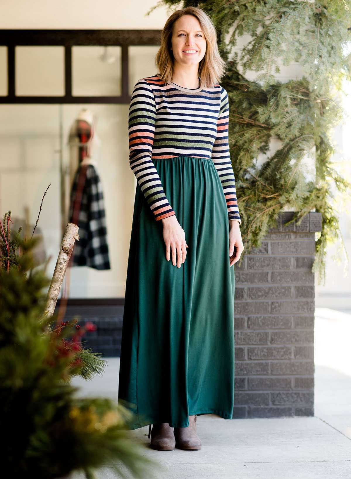 Woman wearing a striped top and solid hunter green bottom maxi dress.