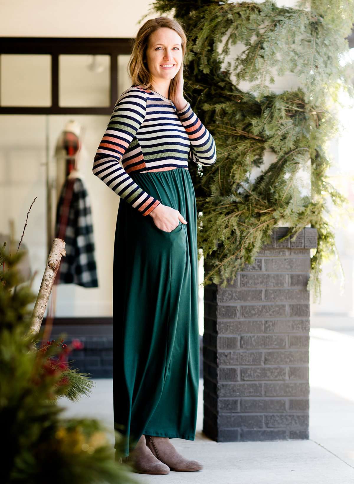 Woman wearing a striped top and solid hunter green bottom maxi dress.