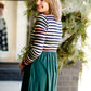 Woman wearing a striped top and solid hunter green bottom maxi dress.