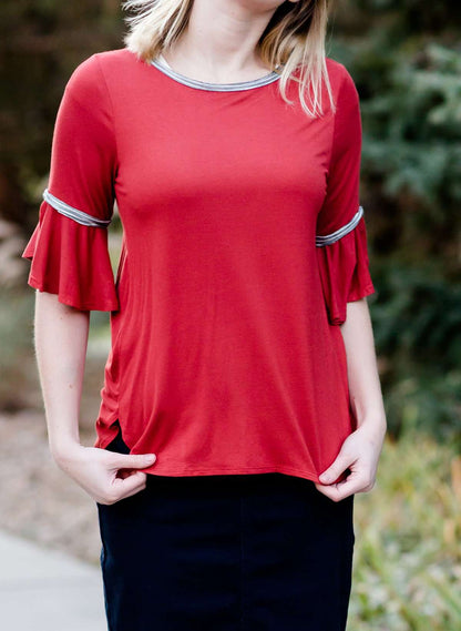 Woman wearing a rust colored, modest bell sleeve top. The 3/4 sleeves flutter and the top is also lined.