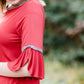 Woman wearing a rust colored, modest bell sleeve top. The 3/4 sleeves flutter and the top is also lined.