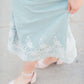 Woman wearing a mint green cotton midi skirt with a self tie and feminine crochet lace detail at the bottom hem