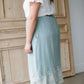 Woman wearing a mint green cotton midi skirt with a self tie and feminine crochet lace detail at the bottom hem