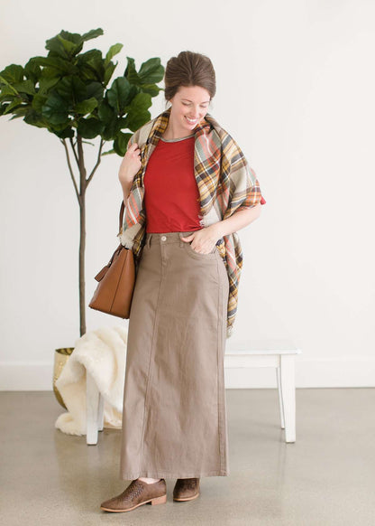 Woman wearing a long khaki twill skirt with a red top and brown braided shoes.