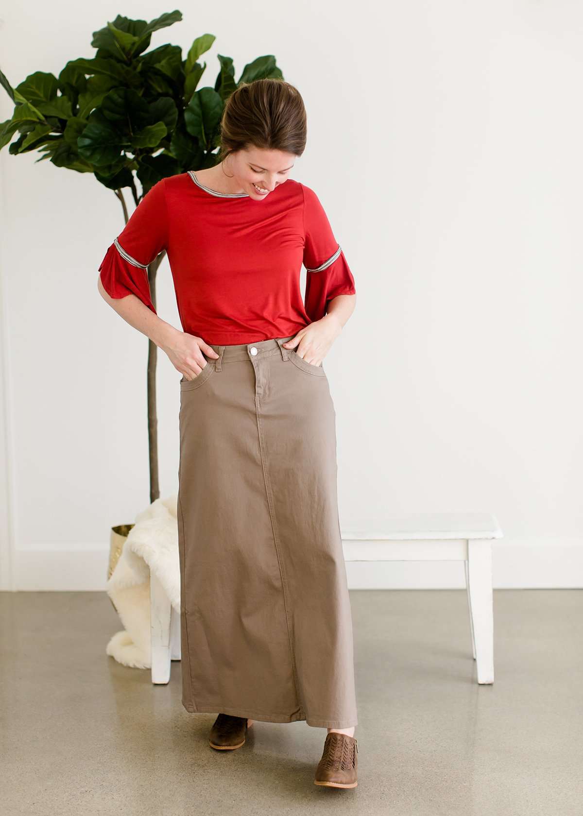 Woman wearing a long khaki twill skirt with a red top and brown braided shoes.