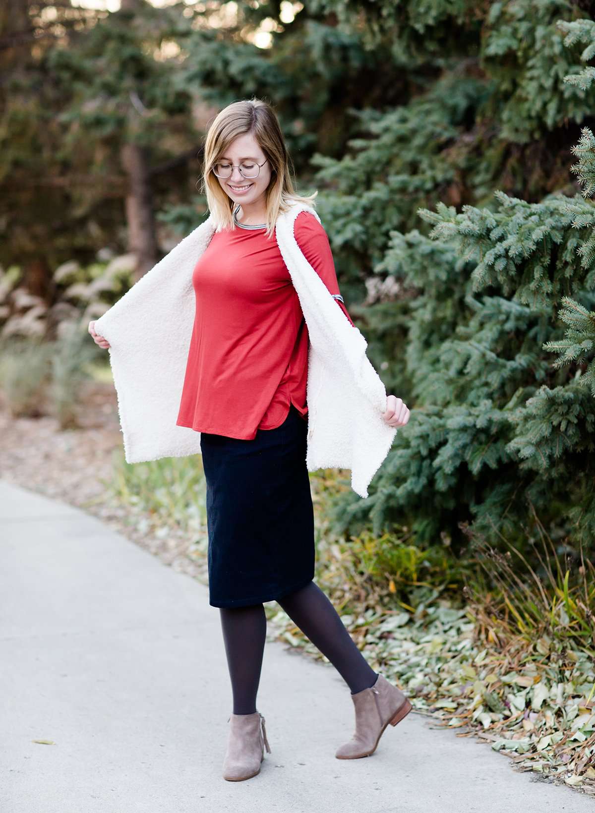 Young woman in a modest black midi skirt wearing a cream colored, soft drape style vest.