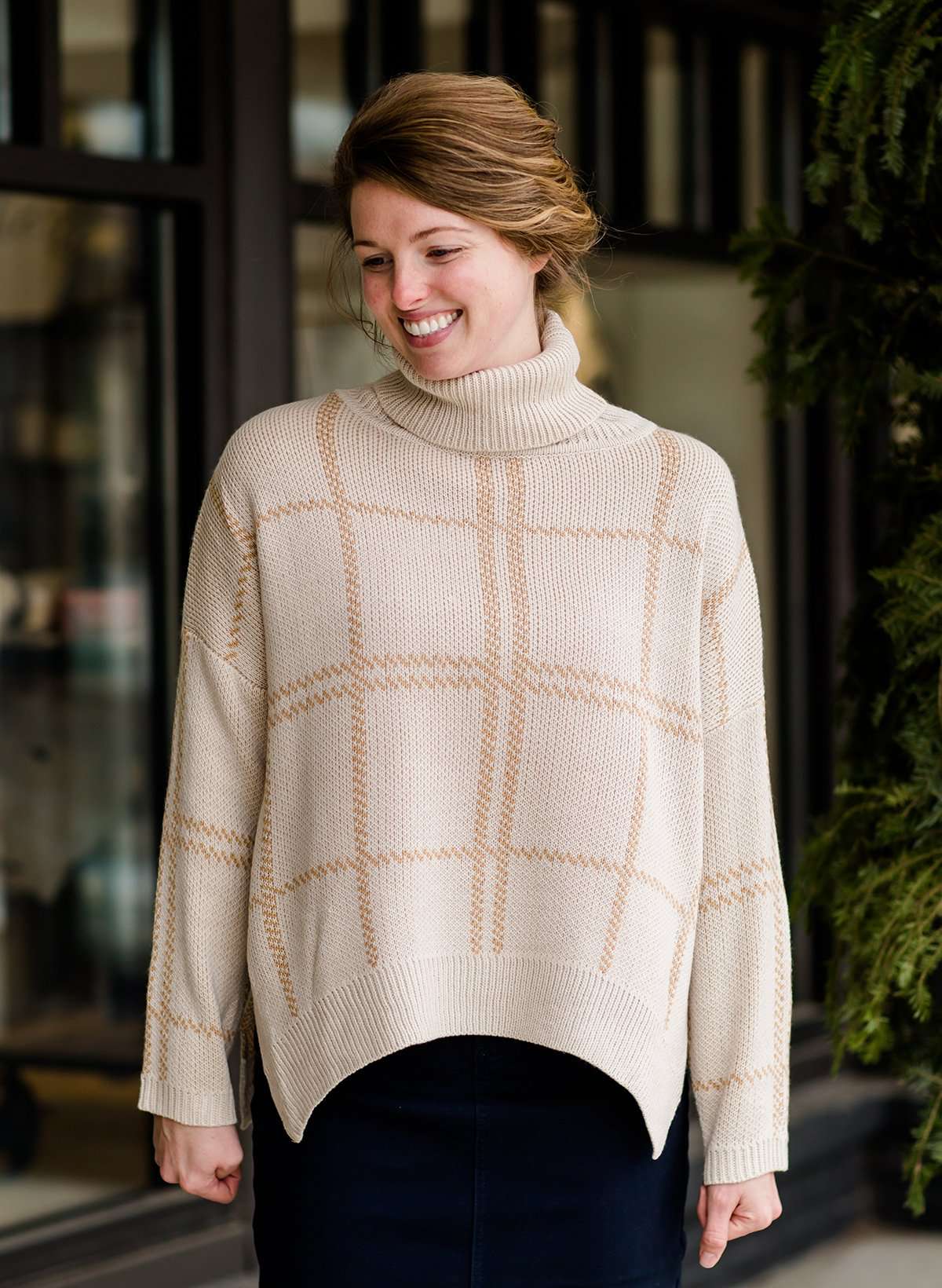 Woman wearing a shawl like sweater that is cream with a gold and orange subtle design.
