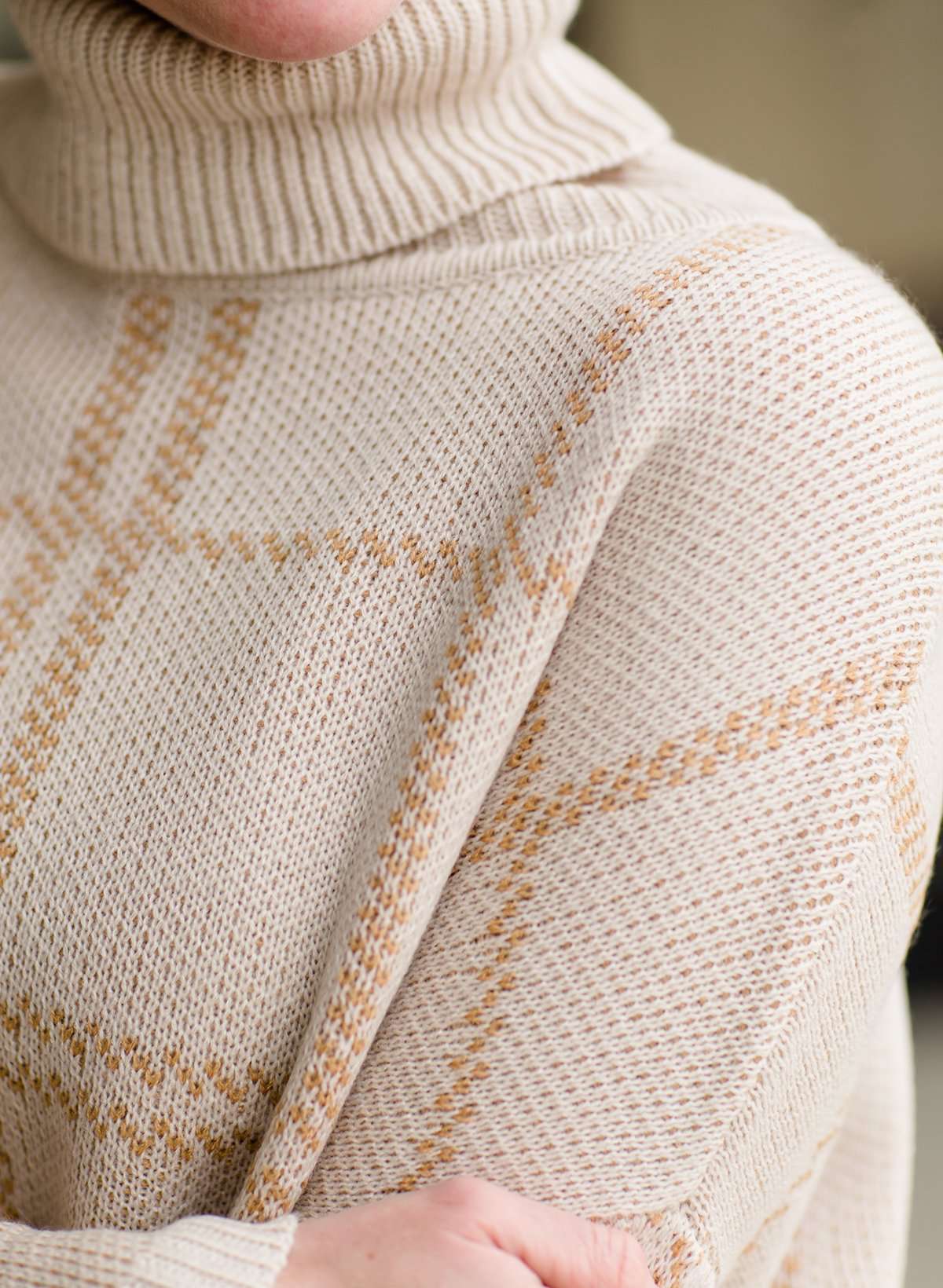 Woman wearing a shawl like sweater that is cream with a gold and orange subtle design.