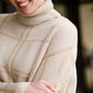 Woman wearing a shawl like sweater that is cream with a gold and orange subtle design.