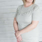 Grey and white striped crew neck tee shirt with a ruffle just above the chest.