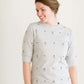 Woman wearing a gray crew neck sweatshirt that is half sleeves and has jewel designs on it.