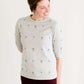 Woman wearing a gray crew neck sweatshirt that is half sleeves and has jewel designs on it.