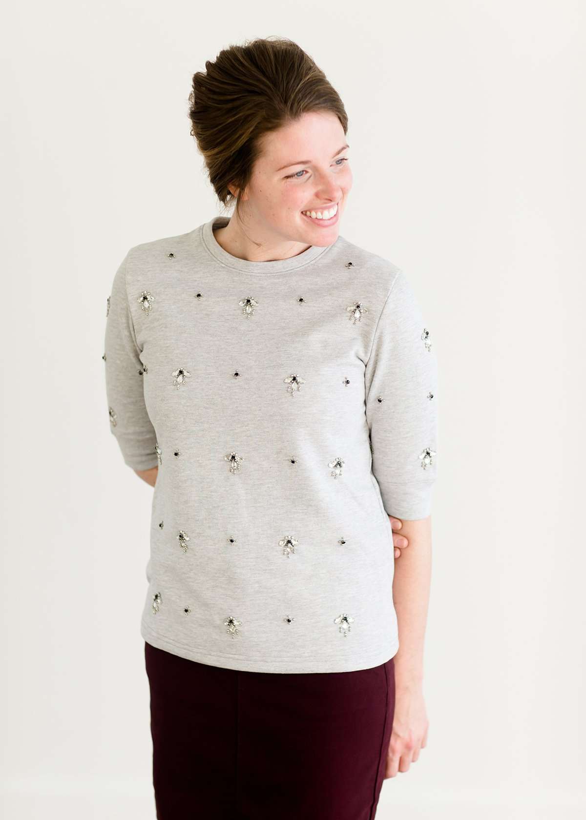 Woman wearing a gray crew neck sweatshirt that is half sleeves and has jewel designs on it.