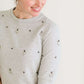 Woman wearing a gray crew neck sweatshirt that is half sleeves and has jewel designs on it.