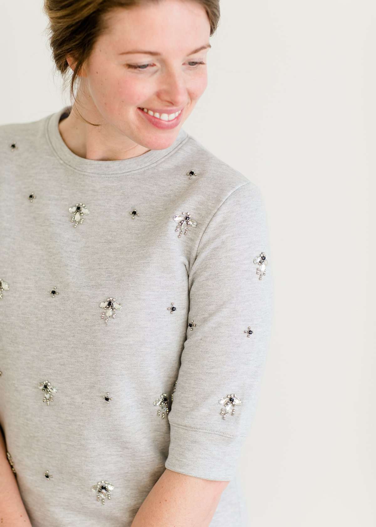 Woman wearing a gray crew neck sweatshirt that is half sleeves and has jewel designs on it.