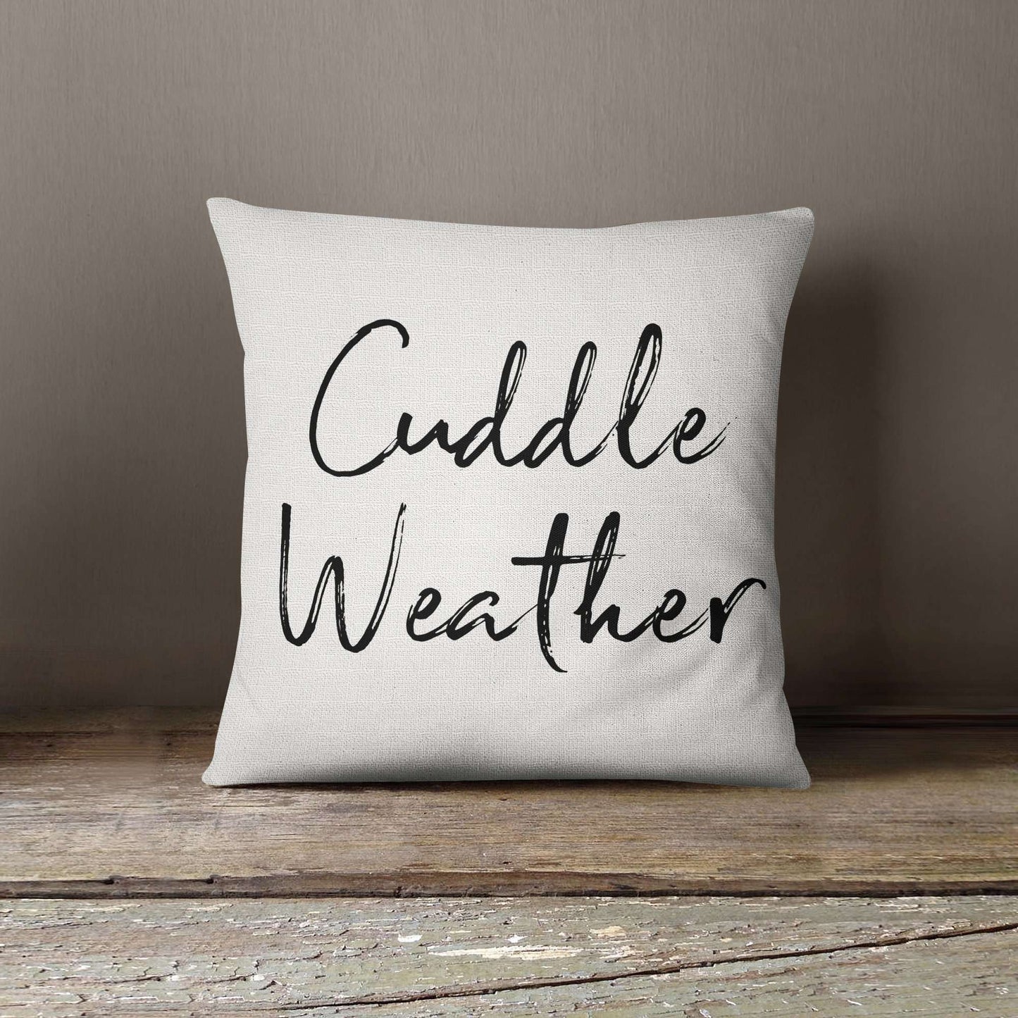 Printed white throw pillow with the script writing 'cuddle weather' on it.