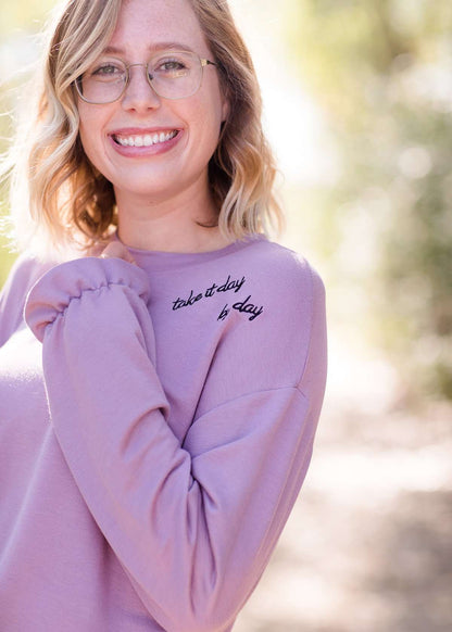 Lavender sweatshirt with ruffle at the end of the sleeves and embroidered up on the left shoulder with "Take it day by day."