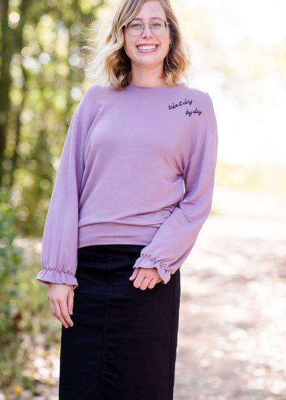 Lavender sweatshirt with ruffle at the end of the sleeves and embroidered up on the left shoulder with "day by day