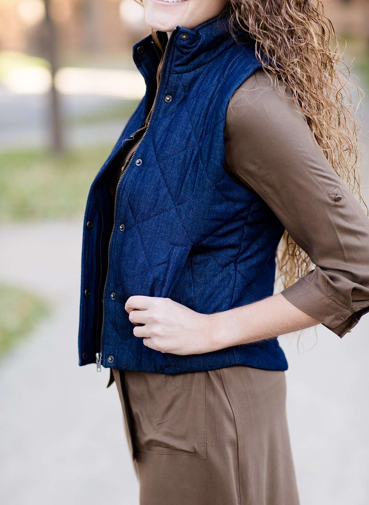Woman wearing a denim quilted modest vest with a plaid and flannel lining.