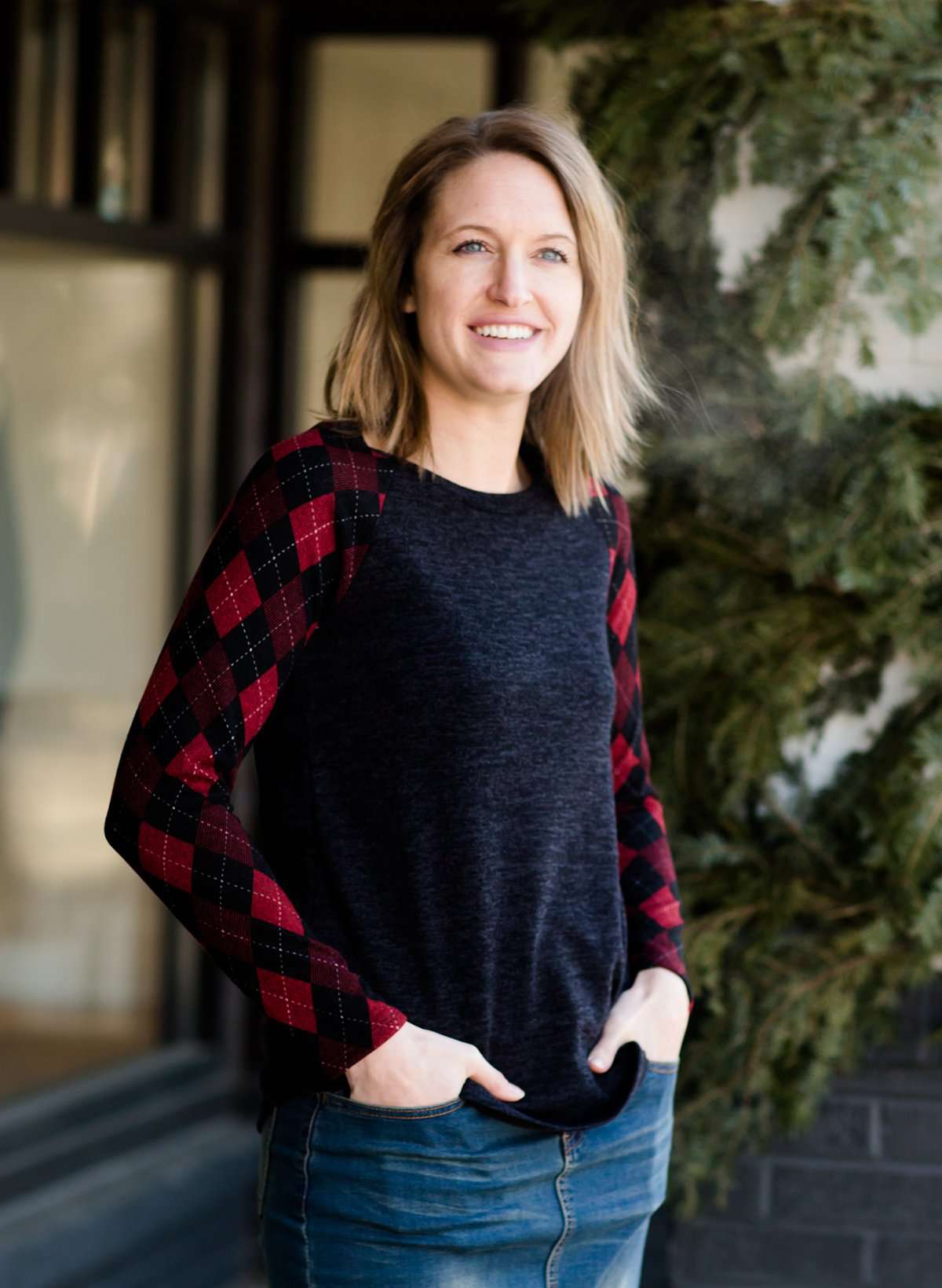 Woman wearing a dark charcoal raglan style top with diamond, argyle checks that are black and red. She is standing outside of Inherit Clothing Company.