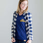 Young woman wearing a blue graphic tee with yellow words that says "Do Good." It is also paired with a below the knee denim skirt and a plaid button up top.