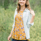 young woman wearing a mustard color tank with blue and white florals. There is embroidered detail just below the chest.