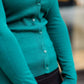 Woman wearing a modest and classic pink, burgandy, emerald and olive colored button up crewneck cardigan with a midi skirt
