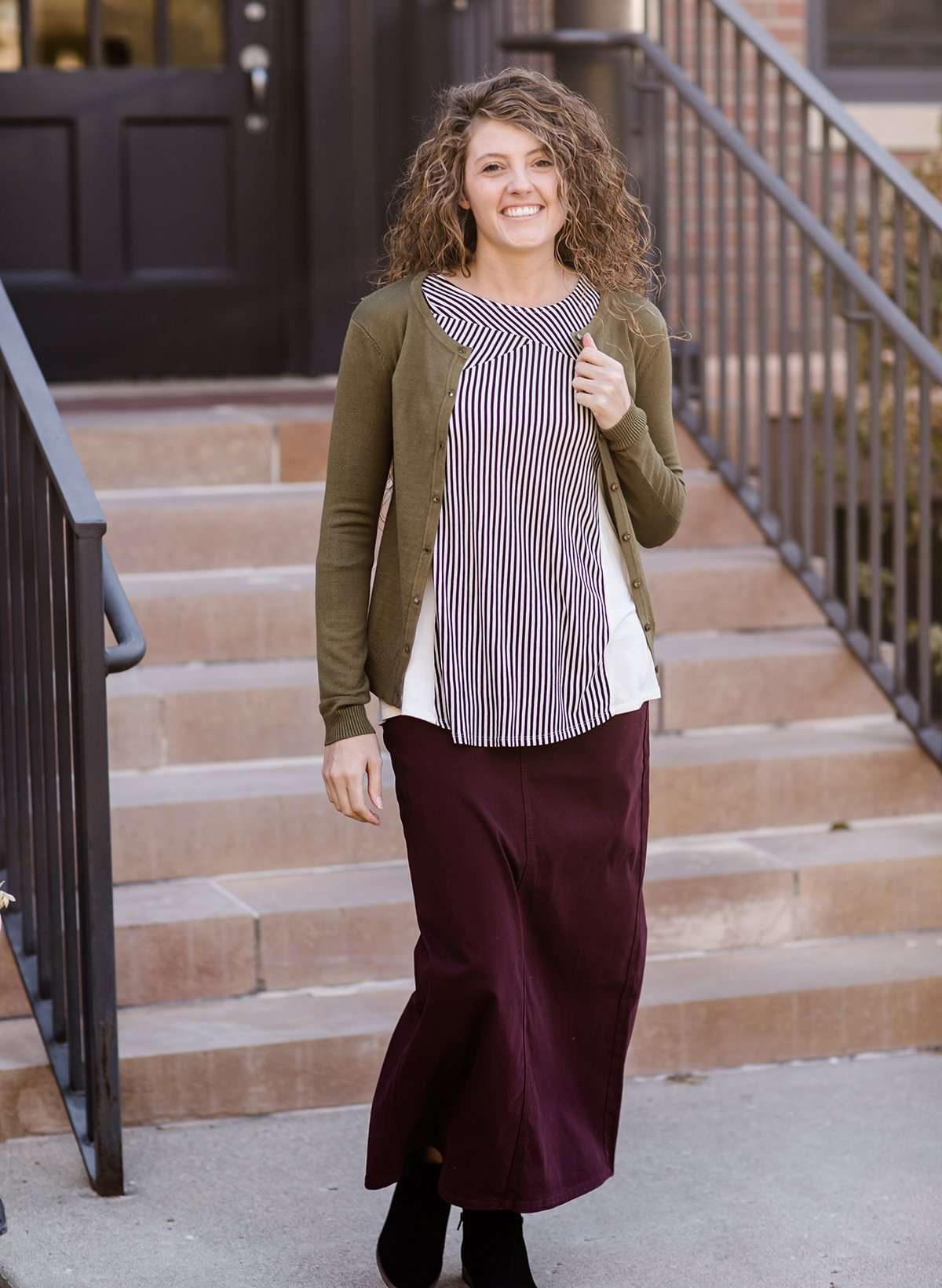 Woman wearing a modest and classic pink, burgandy, emerald and olive colored button up crewneck cardigan with a midi skirt