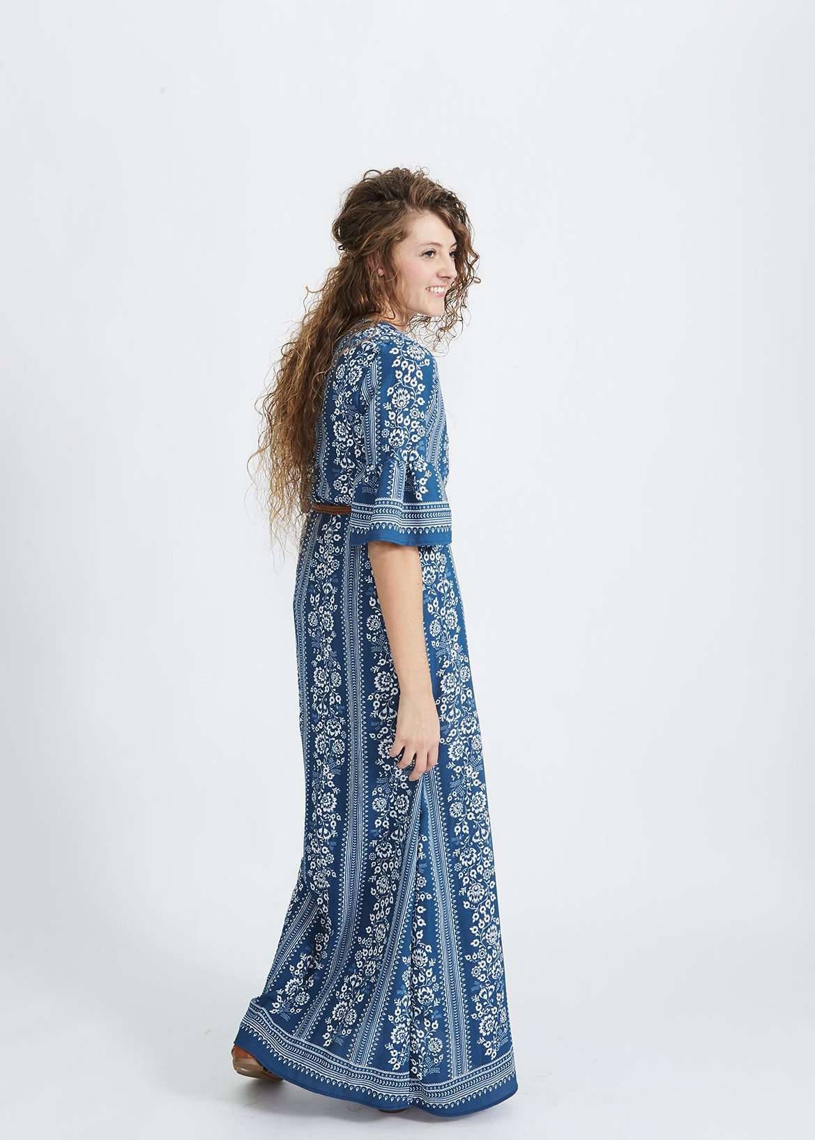 Woman wearing a long bohemian style blue dress with white accent designs and 3/4 trumpet style sleeves.